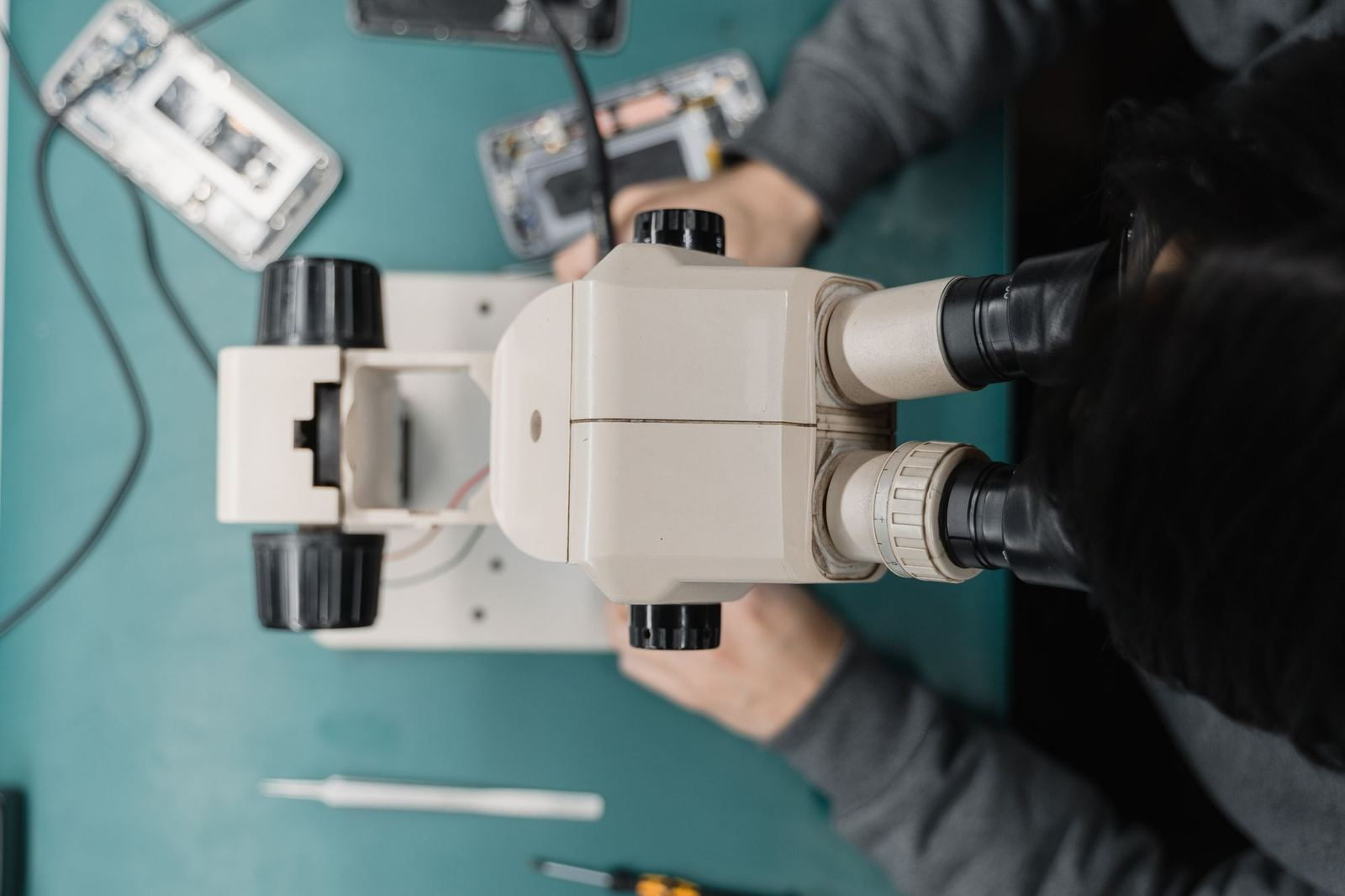 Technician repairing a phone under a microscope at a repair bench